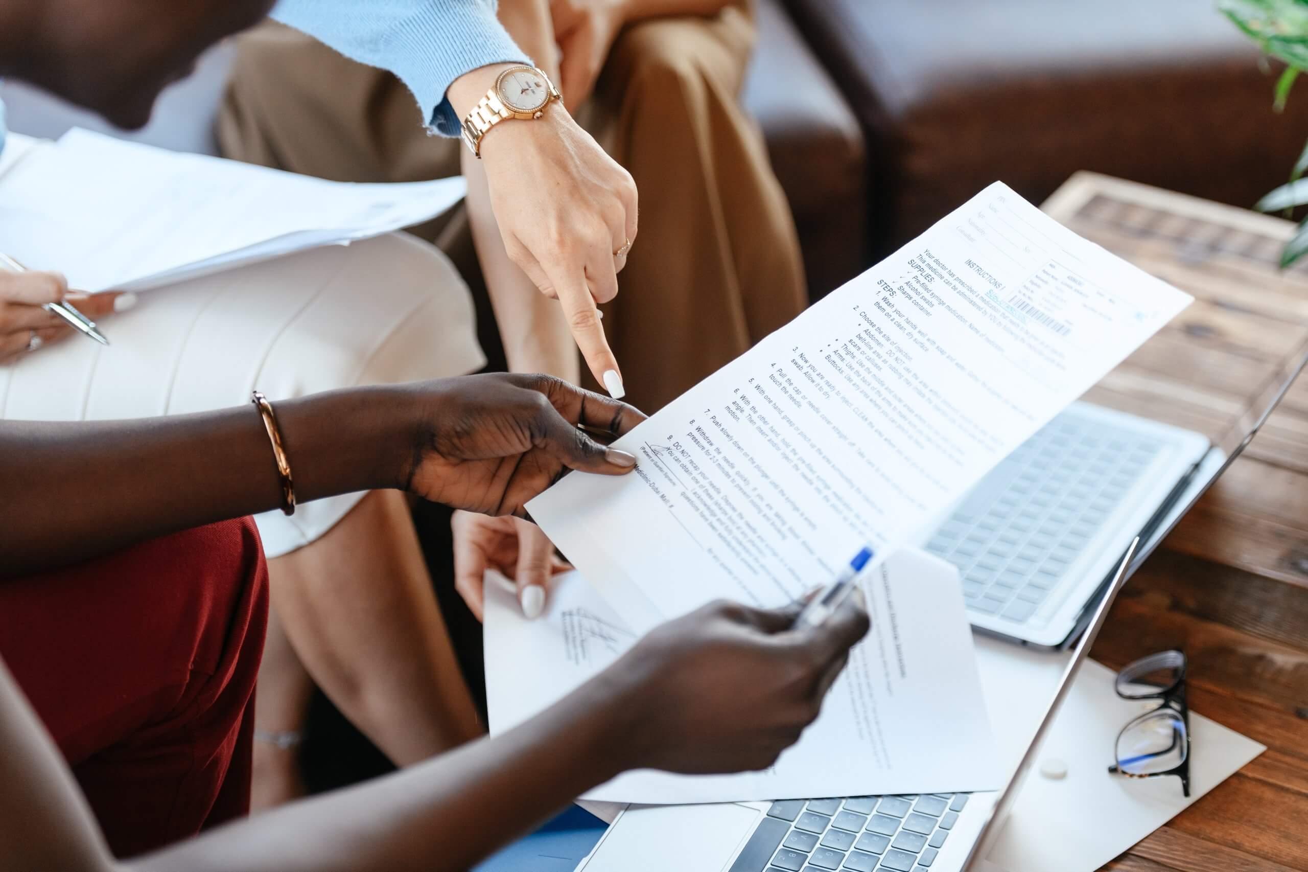 three people discussing something with their laptops and notebooks, two women pointing at notes they are looking at