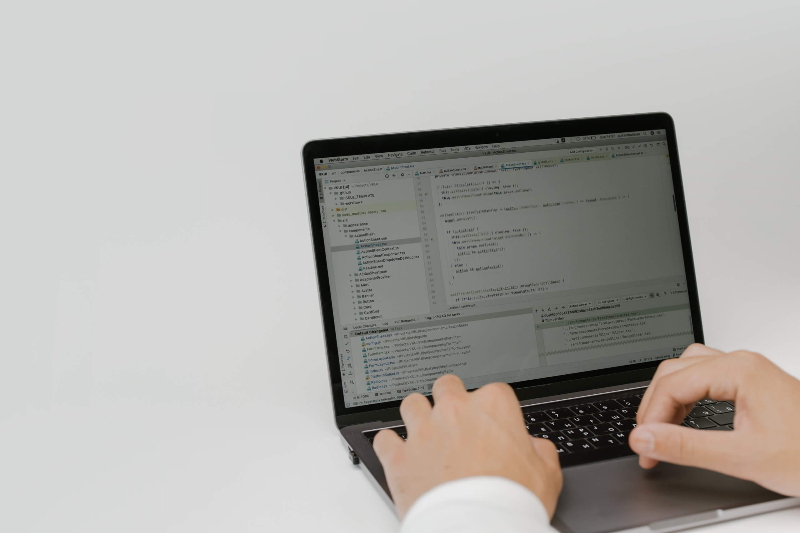 A white desk with a laptop on it, two hands on the laptop's keyboard writing some code