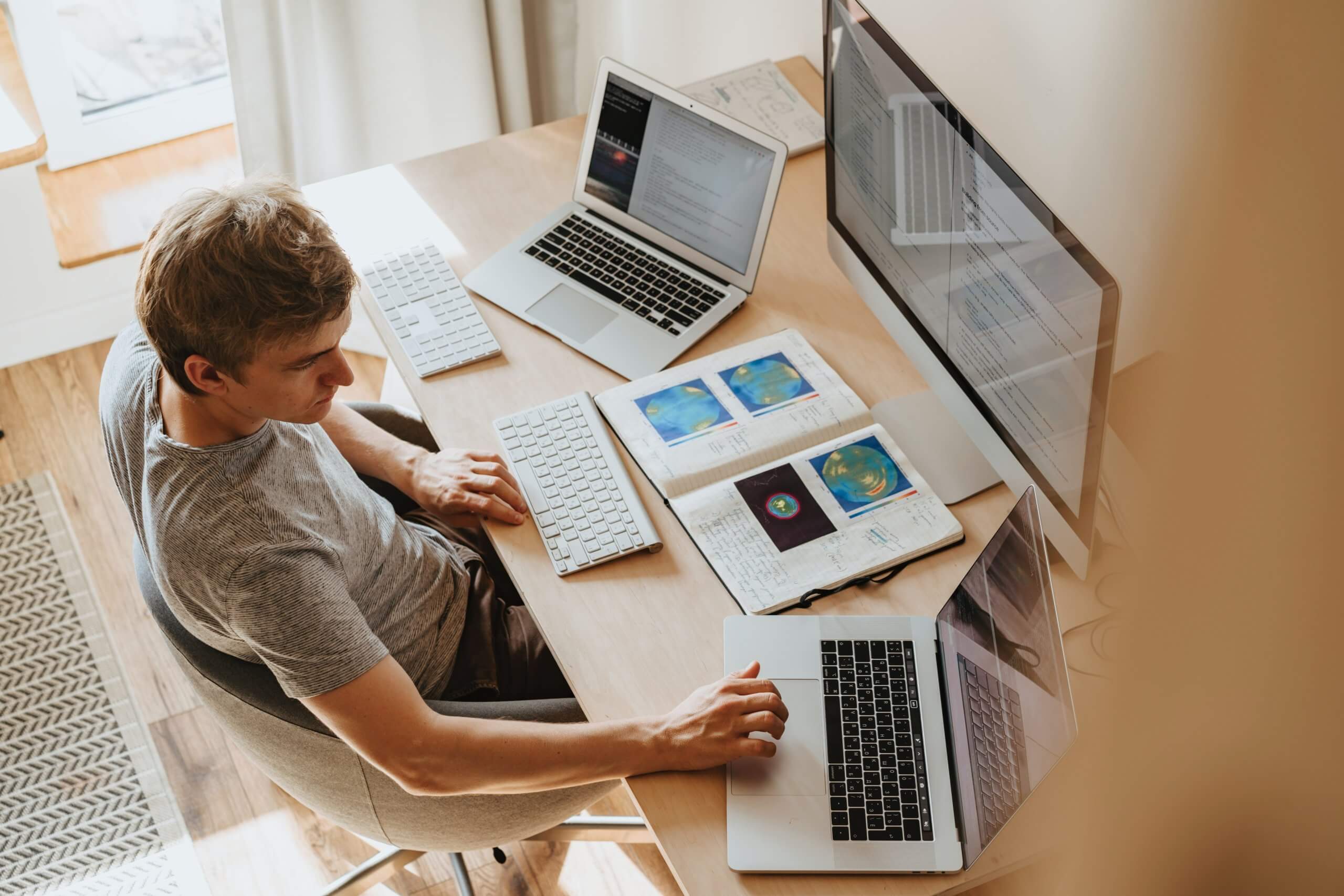 A man sitting at his desk with two laptops and one big screen, two keyboards and a lot of notes, working on some code or something similar