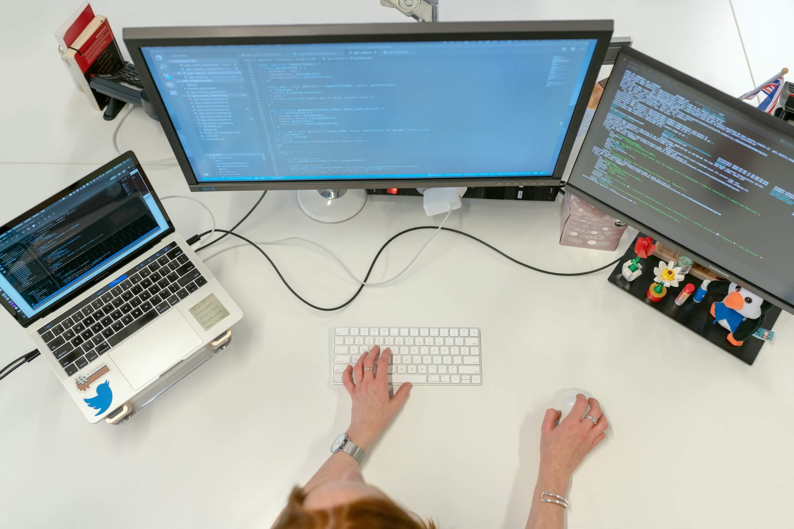 a person is sitting at the desk using two monitors and a laptop and programming